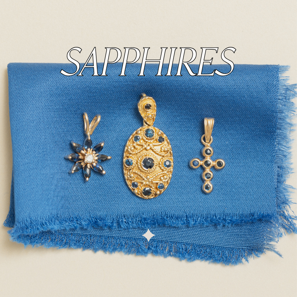Image of vintage, yellow gold sapphire gemstone pendants on satin blue fabric