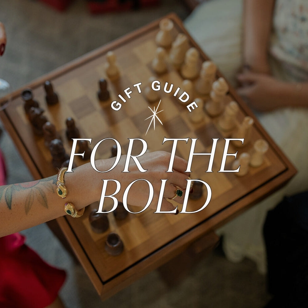 gift guide for the bold text over image of woman playing chess wearing bold gold and gemstone jewellery
