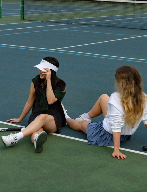 Image of two women casually sitting on the tennis court
