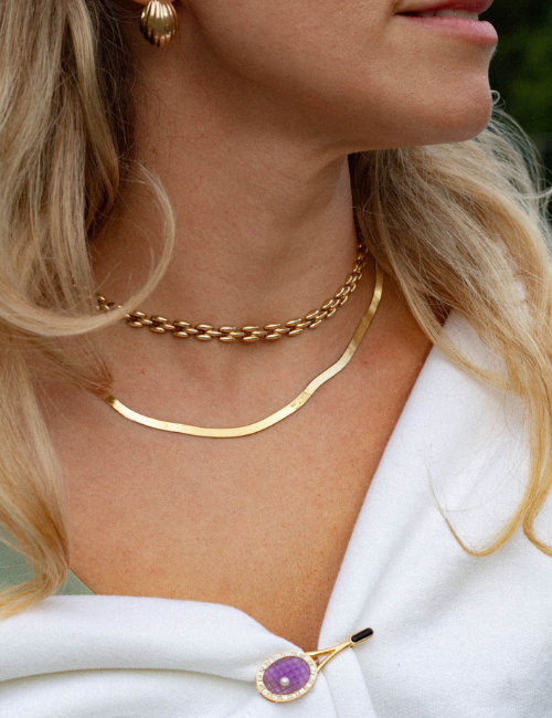 Detail image of woman wearing yellow gold, vintage panther and herringbone necklace stack and purple amethyst tennis racquet brooch