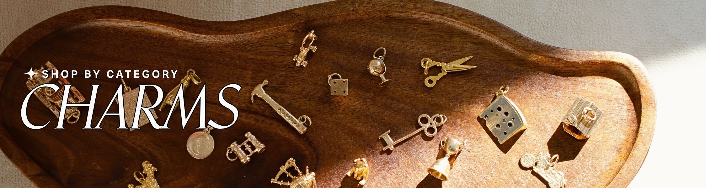 Wooden tray with various gold charms on a light background text over reads: shop by category: charms