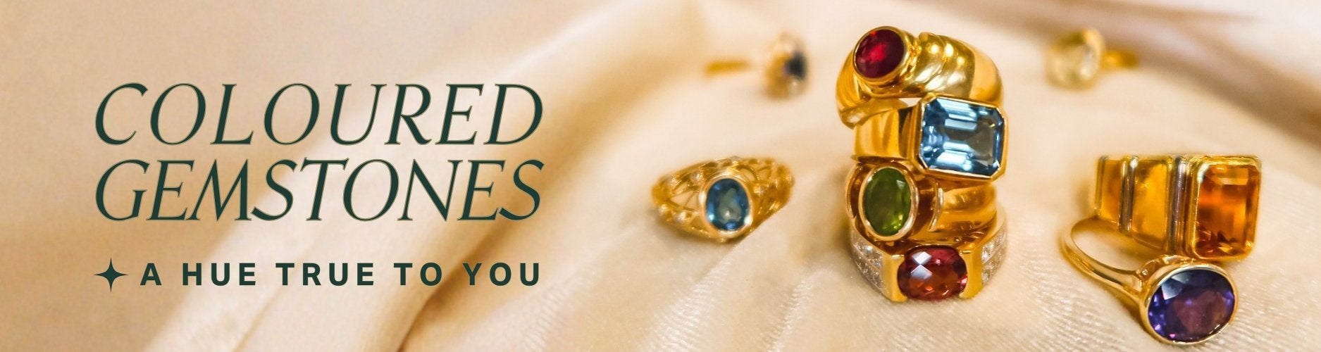 Gold rings with brightly colored gemstones on a beige fabric background, text overlay reads: coloured gemstones, a hue true to you