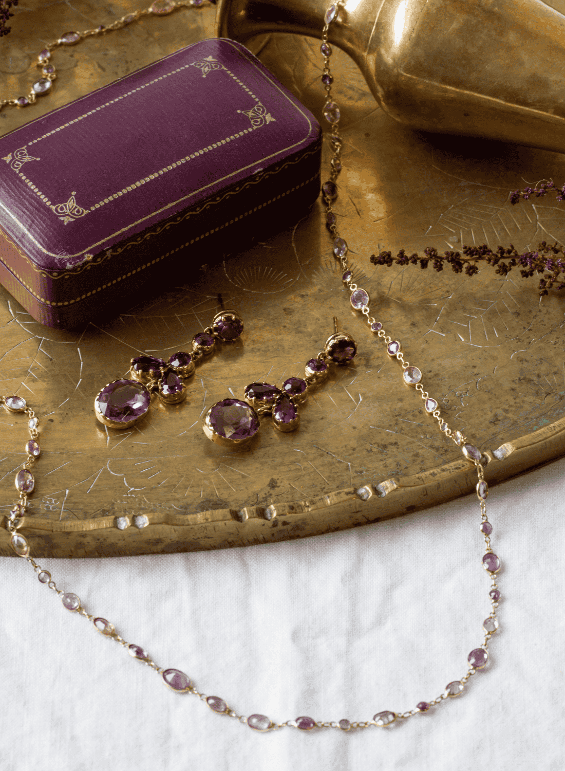 Antique gold amethyst necklace and matching drop earrings styled on an engraved brass tray beside a vintage jewellery box, featuring February birthstone pieces.