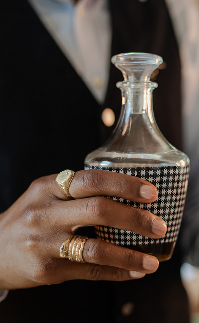 Vintage and preloved men’s jewellery, featuring gold rings styled on a hand holding a glass decanter.