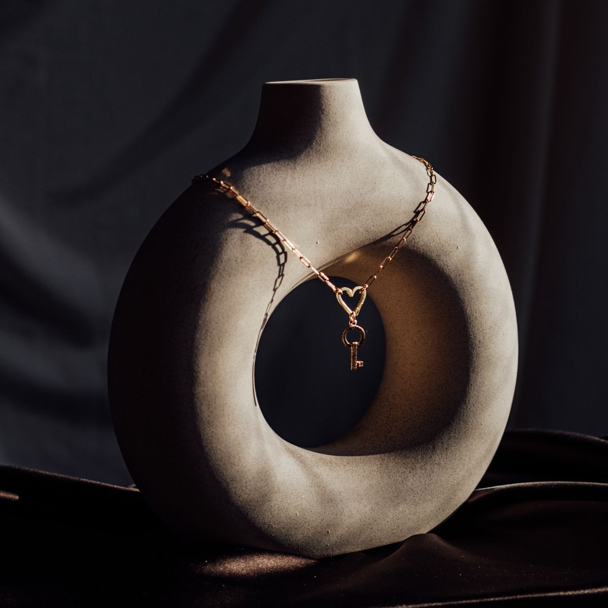 Organic, textured round donut vase with paperclip chain draped over connected by heart charm clasp and vintage key charm.