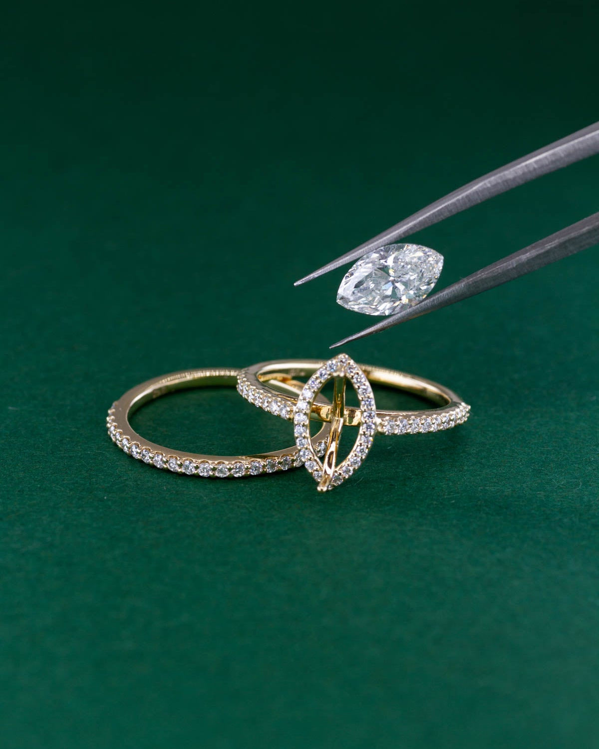 Gold ring with diamond being adjusted by tweezers on a green background
