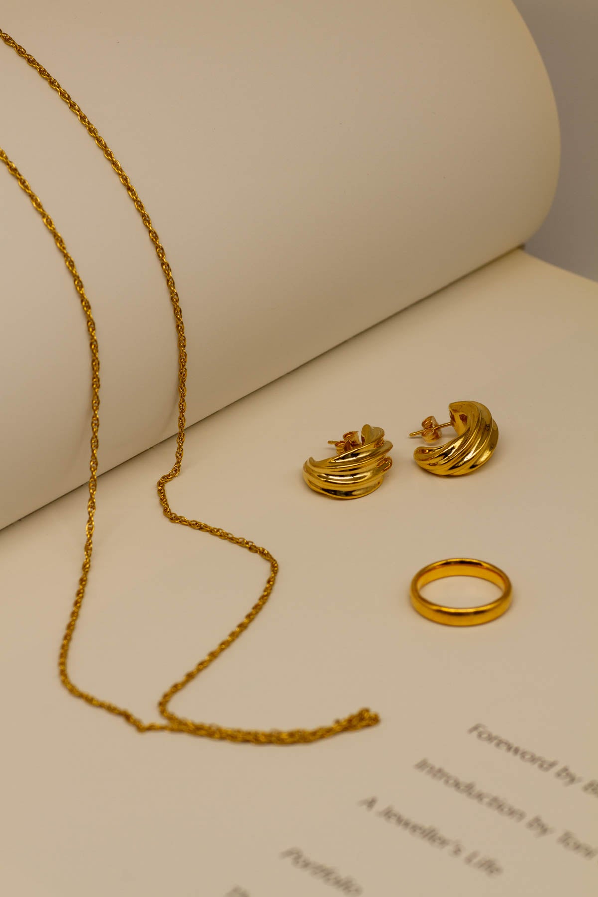fine gold jewelry on an open book, a chain draped accross the pages, hoop earrings and a simple gold band