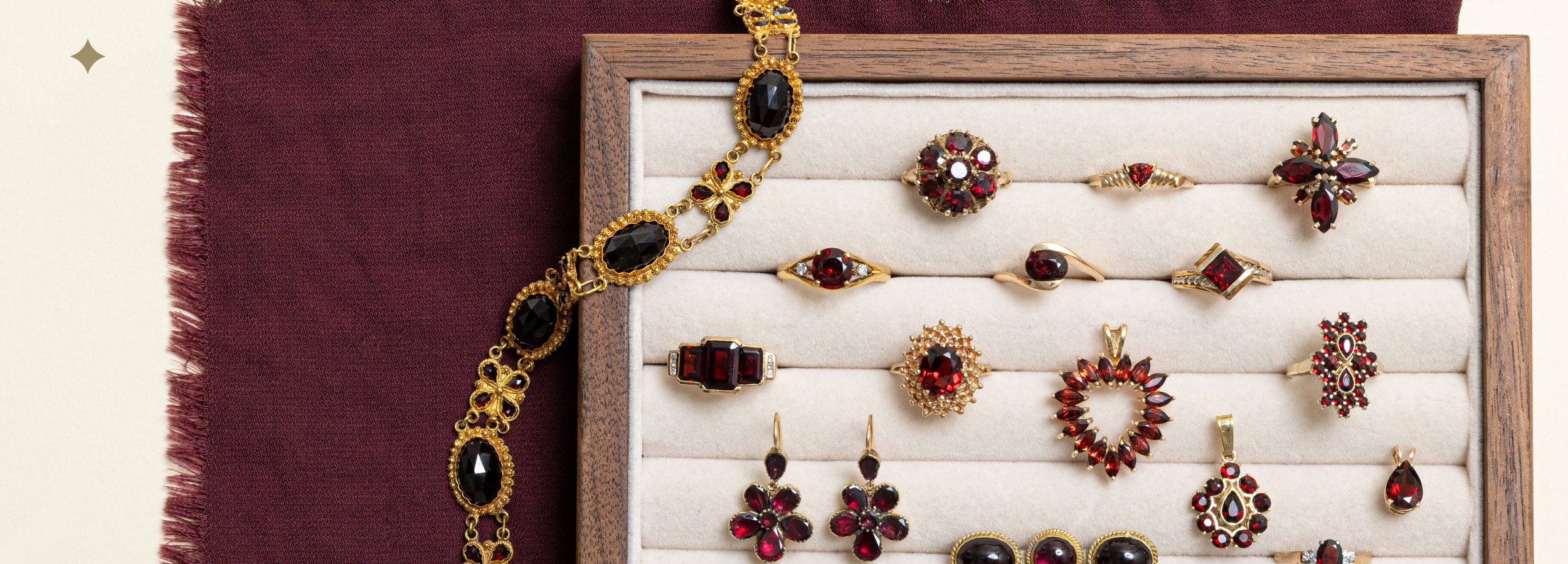Vintage garnet jewellery laid on burgundy fabric, featuring gold garnet bracelet, earrings, and pendants in deep red tones.