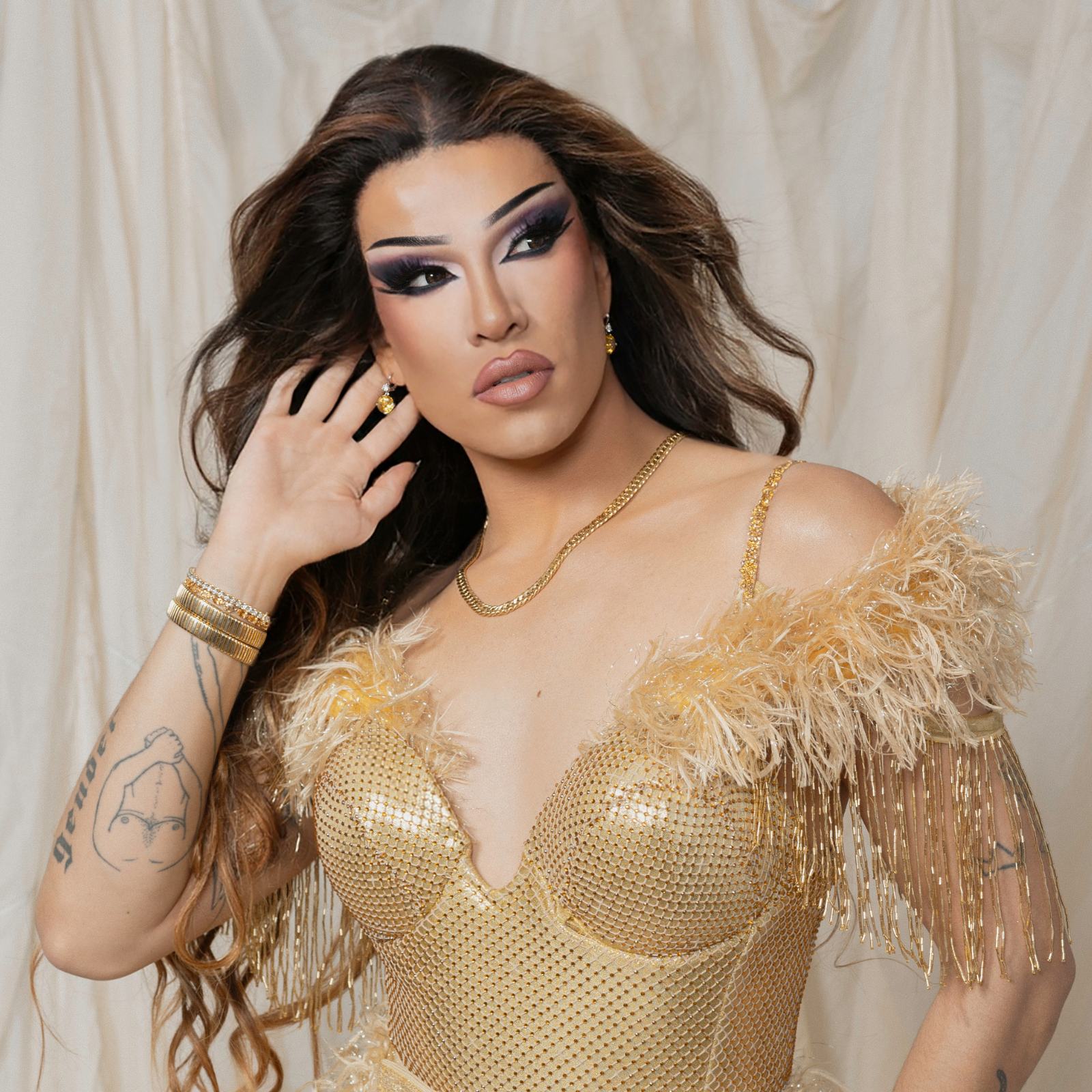 Vancouver-based performer, host, model, and 2SLGBTQIA+ activist, Kendall Gender, wearing a glamorous gold outfit adorned with feathers and fringe, showcasing curated preloved jewelry including gold hoop earrings, a chain necklace, and layered bracelets. The look exudes elegance and individuality, reflecting the spirit of the artist's specially curated vintage collection.