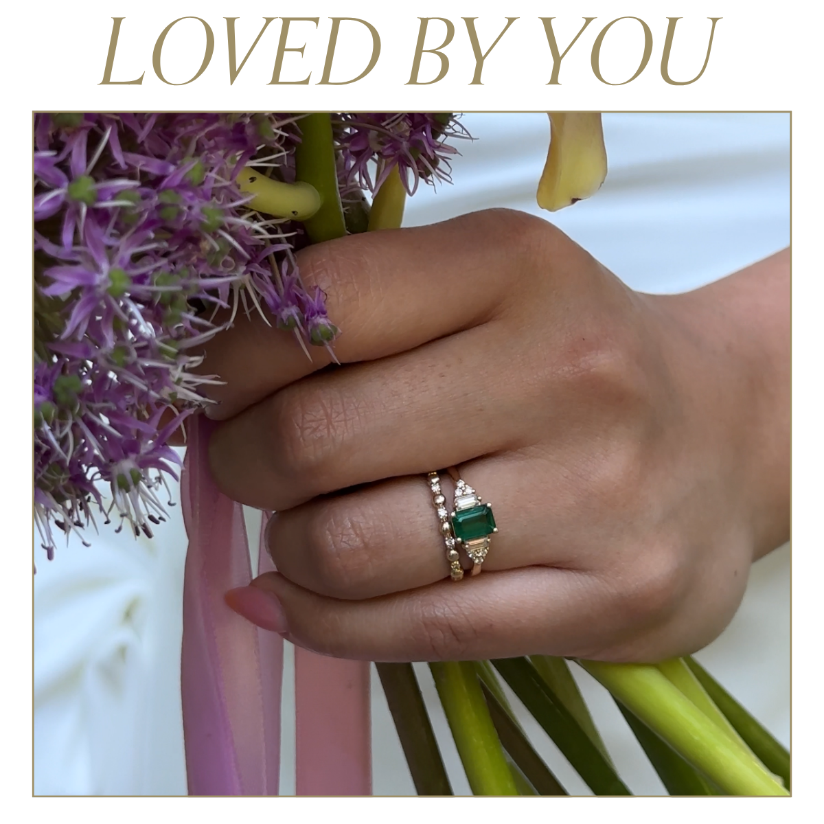 Bride holding a floral bouquet with a close up image of the ring featuring a synthetic emerald engagement ring and alternating gold and diamond wedding band. Text reads: Loved by you
