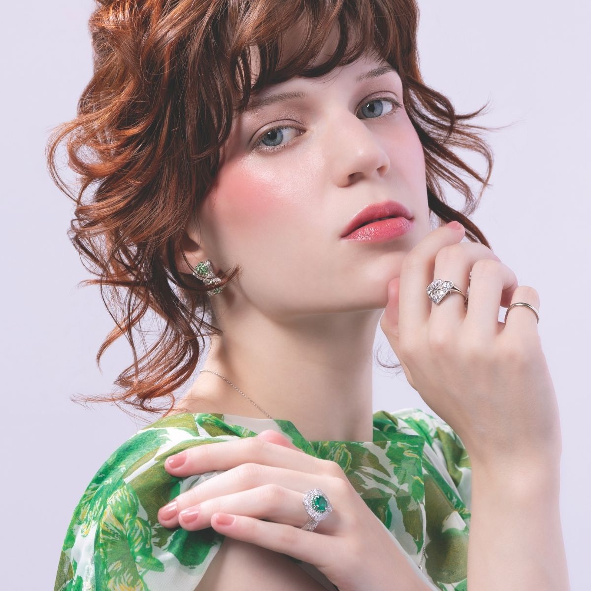 Model with red hair wearing a floral green dress, styled with a cocktail emerald ring and diamond drop earrings.