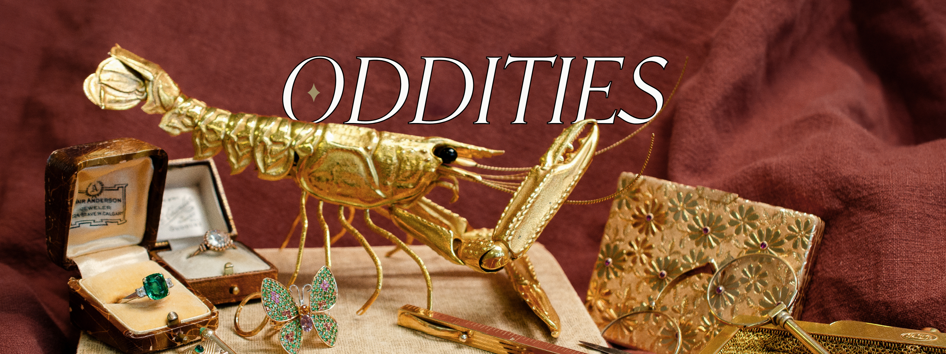Solid gold crayfish-shaped jewelry piece, surrounded by unique, vintage, rare jewelry artifacts with 'Oddities' text on a maroon background