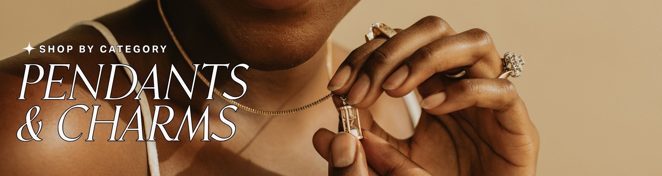 Person holding an hourglass pendant on a gold chain with text 'shop by category: Pendants & Charms' on a beige background