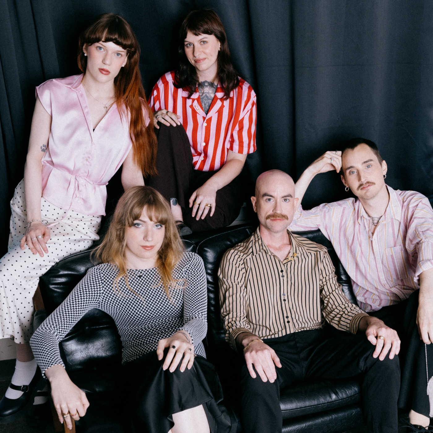 Five people posing together in front of a black curtain backdrop, wearing vintage, preloved jewellery.