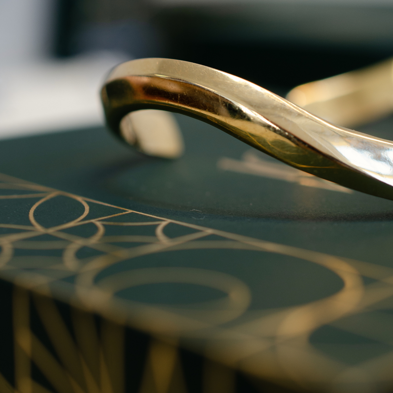 Minimal, yellow gold bangle styled on top of dark green jewellery box with art deco outlines