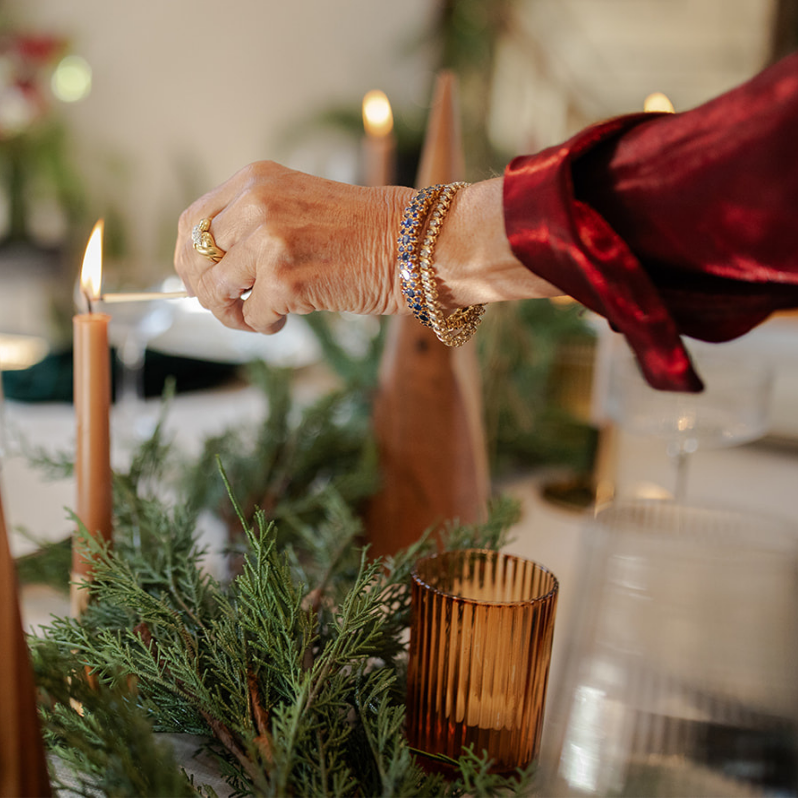 Elegant hand lighting candles while wearing vintage gold tennis bracelets, sapphire bracelet, and antique ring — a warm holiday moment featuring preloved fine jewellery.