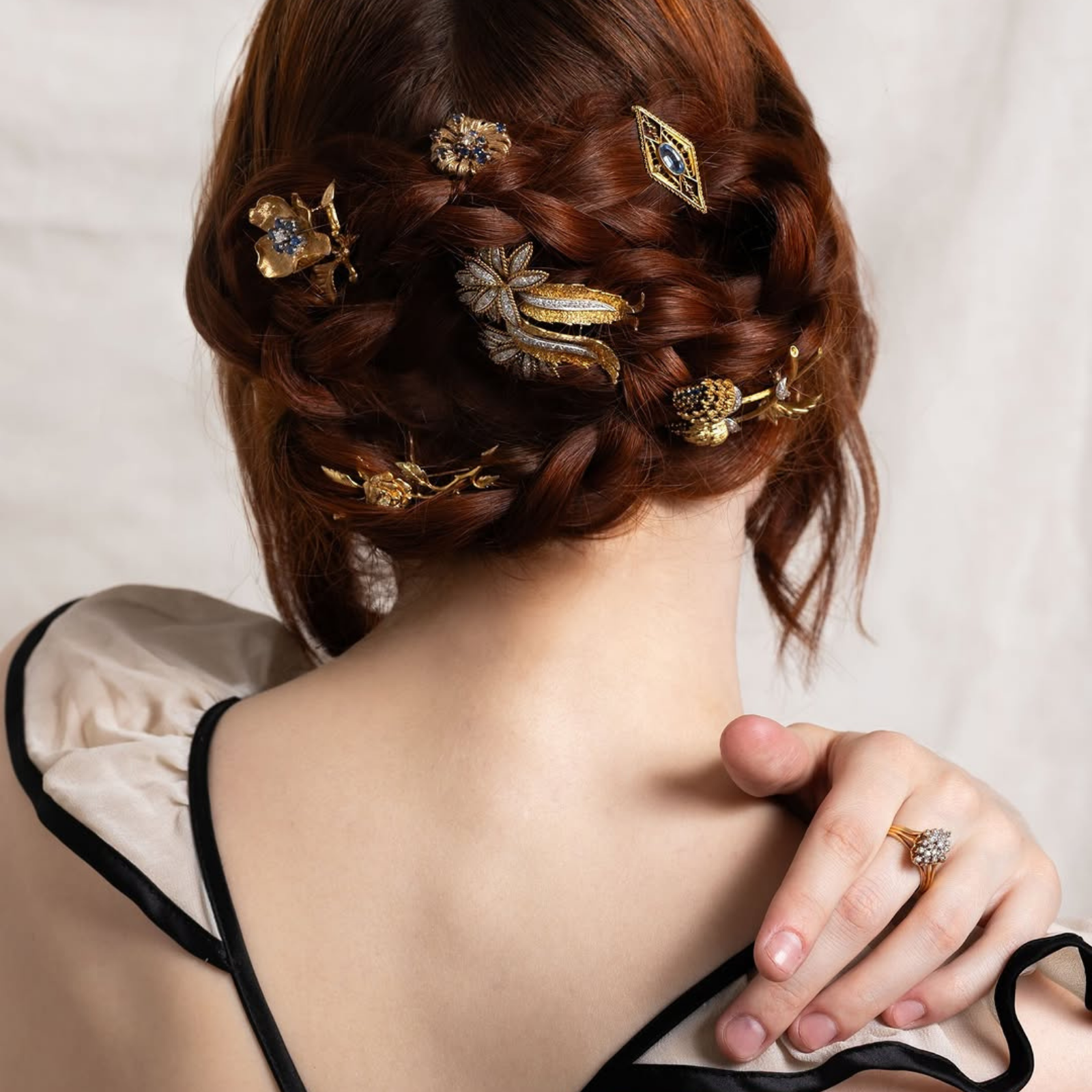 Back of a woman with braided red hair elegantly styled with multiple preloved vintage gold, diamond, and gemstone brooches worn as hair accessories.