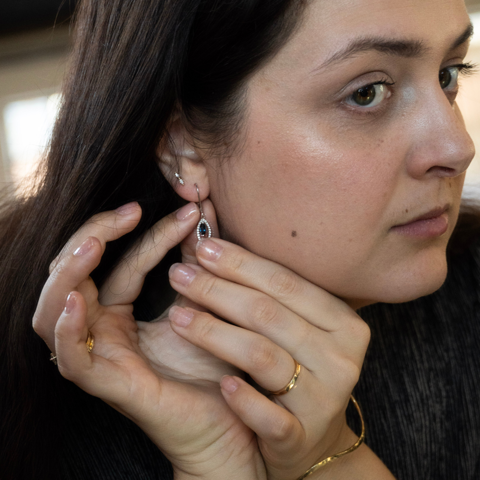 Close-up profile of a woman trying on a preloved fine jewelry marquise blue gemstone dangle earring surrounded by diamonds.