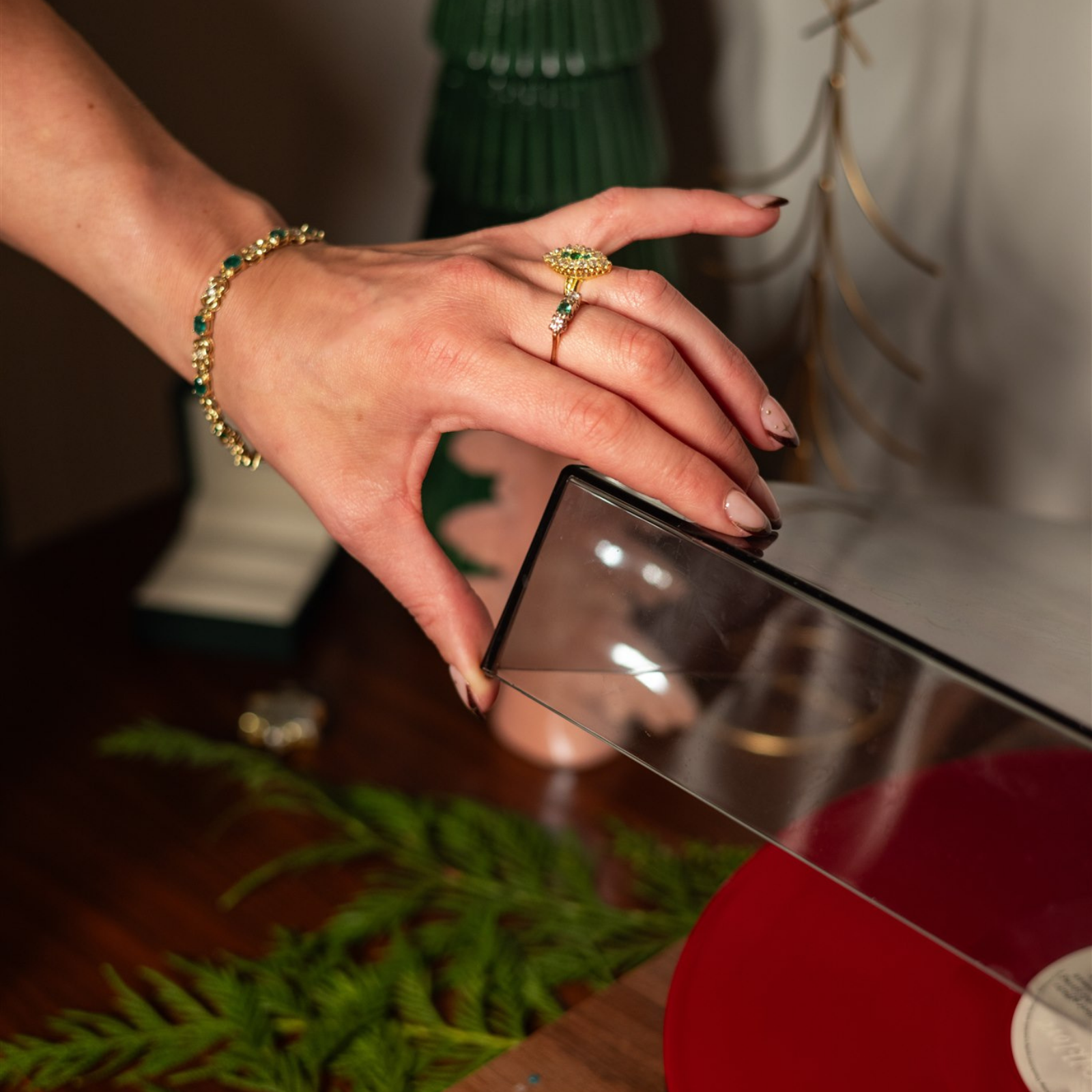 vintage emerald green gemstone rings and matching bracelet, reaching for a record player — preloved fine jewellery styled for holiday gatherings.