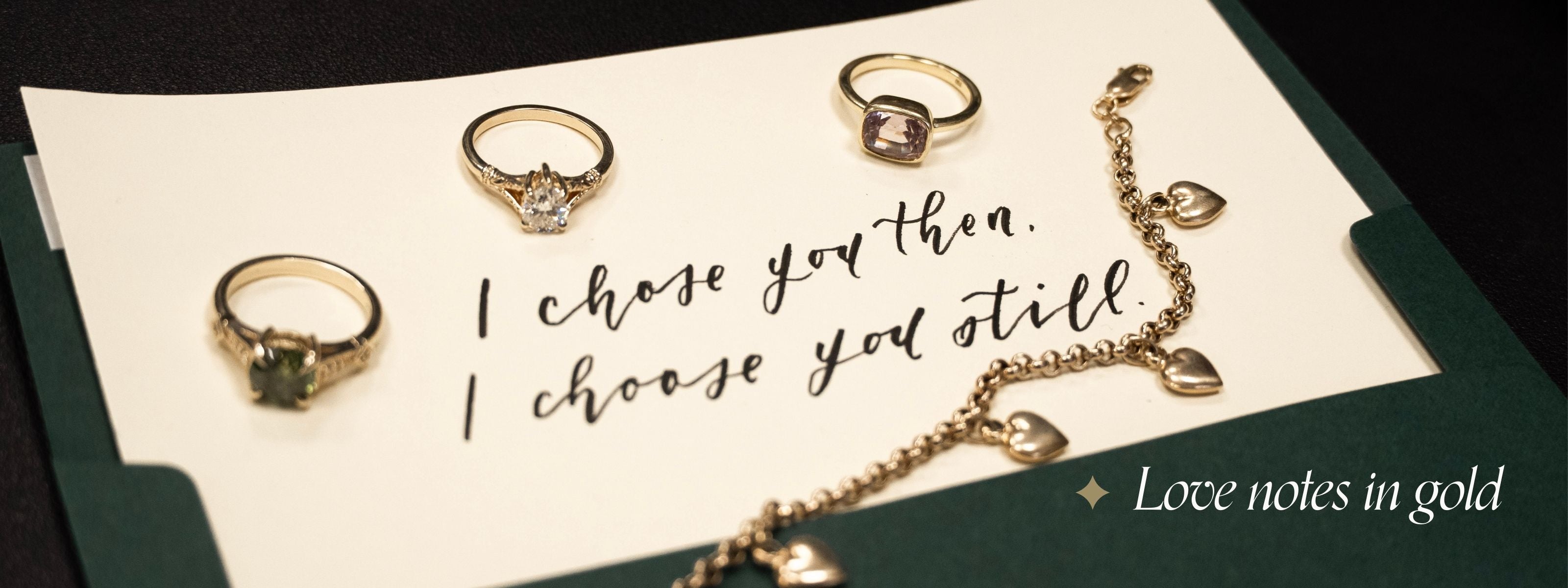 Green envelope with vintage, antique rings and heart charm bracelet scattered. Letter reads: I chose you then, I choose you still. Text reads: Love notes in gold.