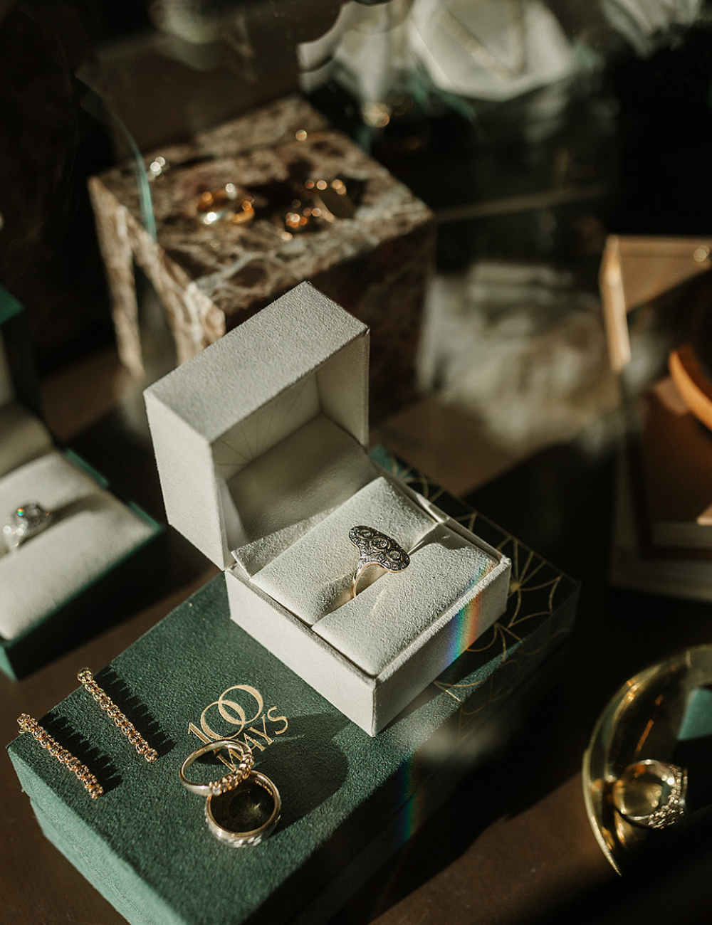 Vintage gold and art deco inspired diamond rings displayed in an open jewellery box beside a green 100 Ways velvet box, styled still life of preloved fine jewellery