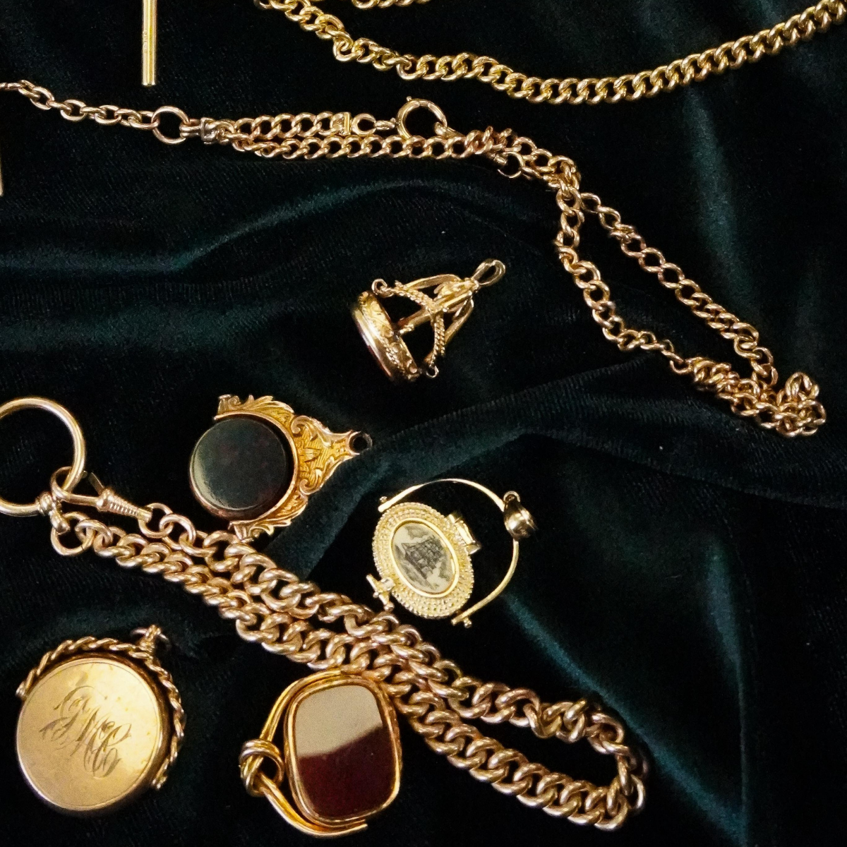 Assortment of vintage gold watch fobs, seal rings, and chains displayed on dark green velvet—classic preloved jewellery pieces rich with history and character.