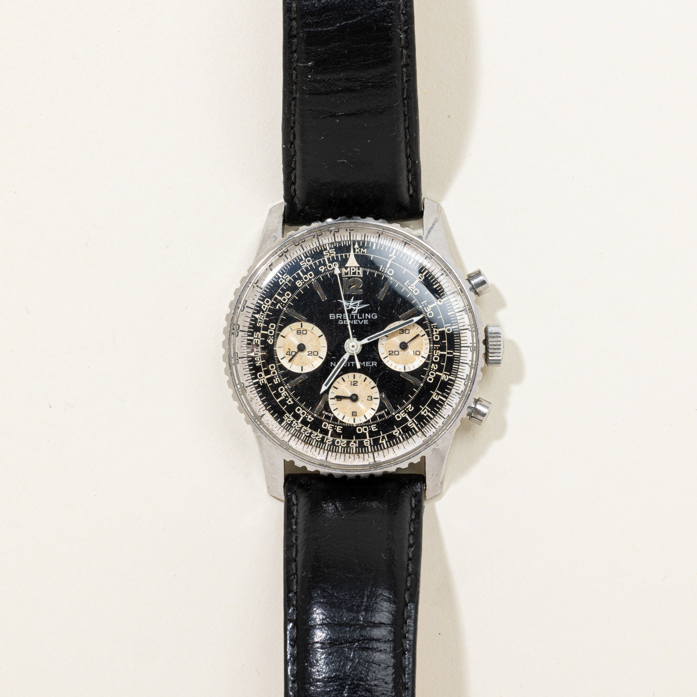 A vintage Breitling chronograph wristwatch with a black dial, silver-tone case, and a black leather strap, shown against a plain off-white background.
