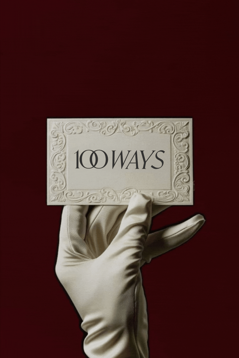 Ornate 100 Ways jewellery card held in a gloved hand against a deep red background, evoking a romantic love letter theme for a Valentine’s Day. Text reads: Written once, worn forever.