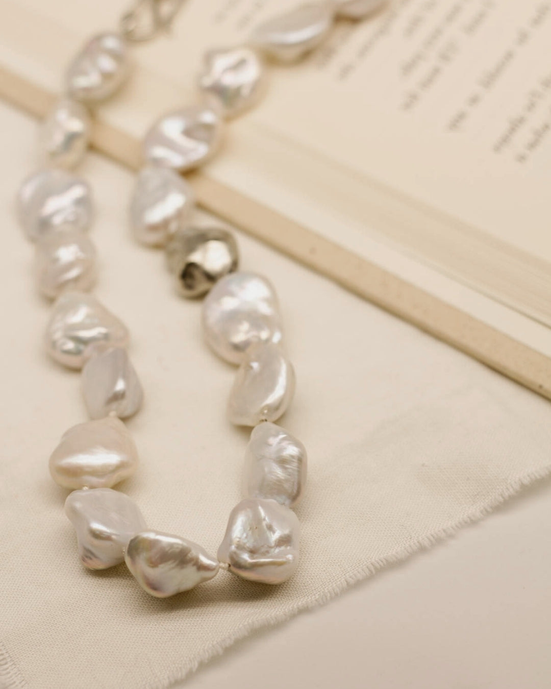 string of baroque pearls on textured fabric and open book