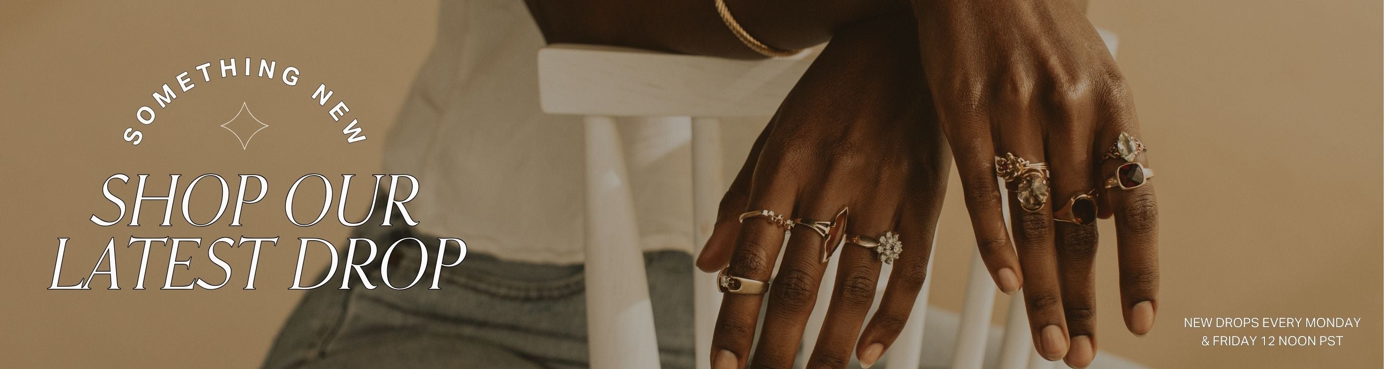 Hand with rings on a blurred background with text overlay: something new, shop our latest drop: new drops every monday & friday 12 noon pst
