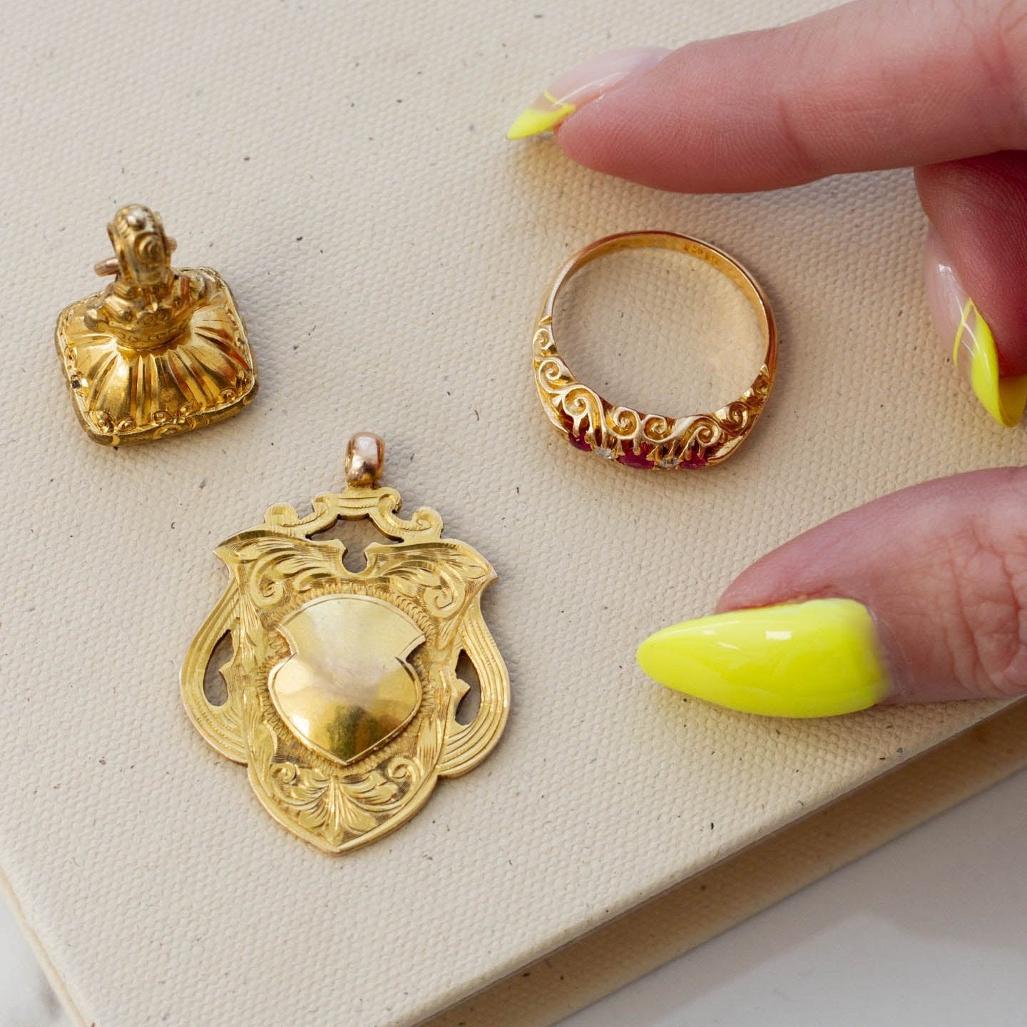 image of woman with brightly coloured nail polish selecting an ornate ruby ring from a tray with other vintage gold jewellery pieces