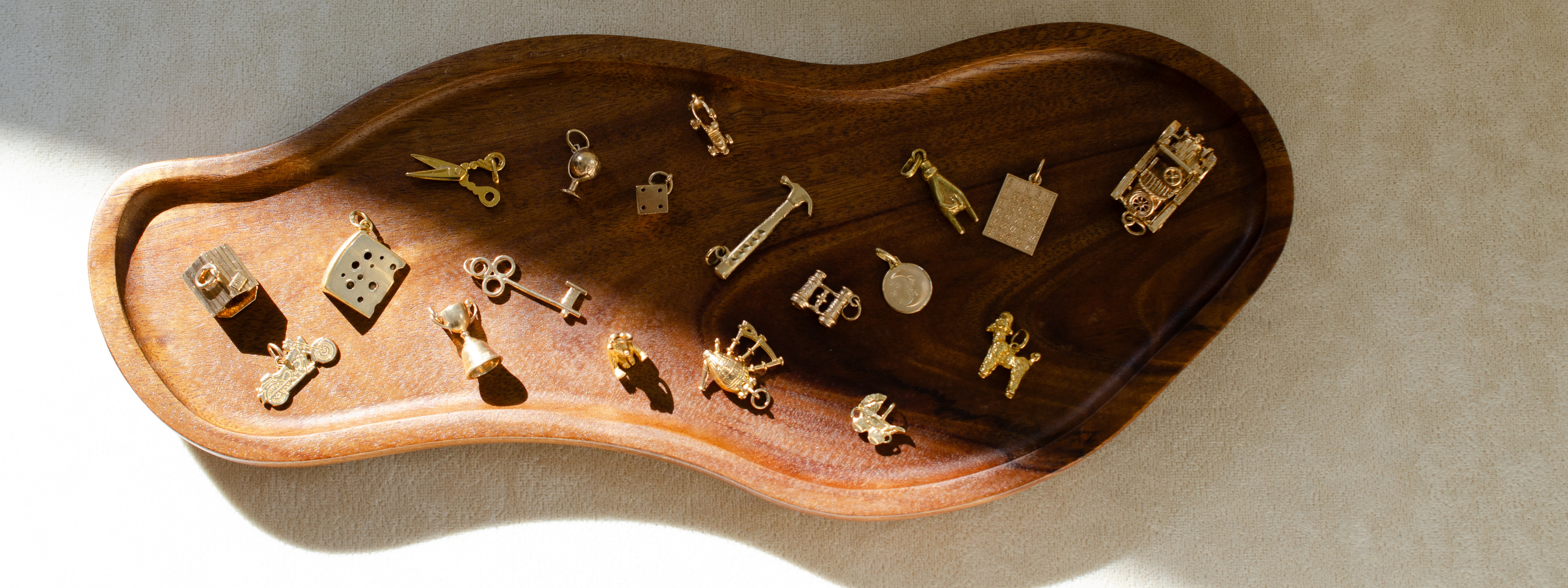 Organic shaped wooden tray with an assortment of vintage, yellow gold charms