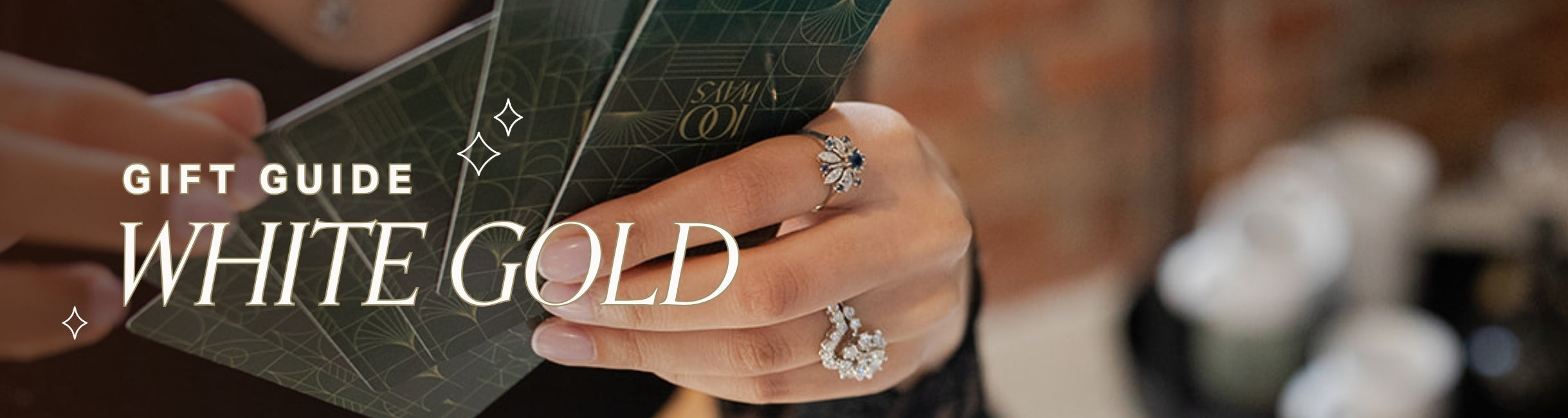 a woman's hands wear white gold and diamond jewellery are seen holding playing cards. text overlay reads gift guide: white gold
