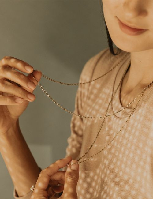 image of woman in filtered light, playing with fine gold chain necklaces