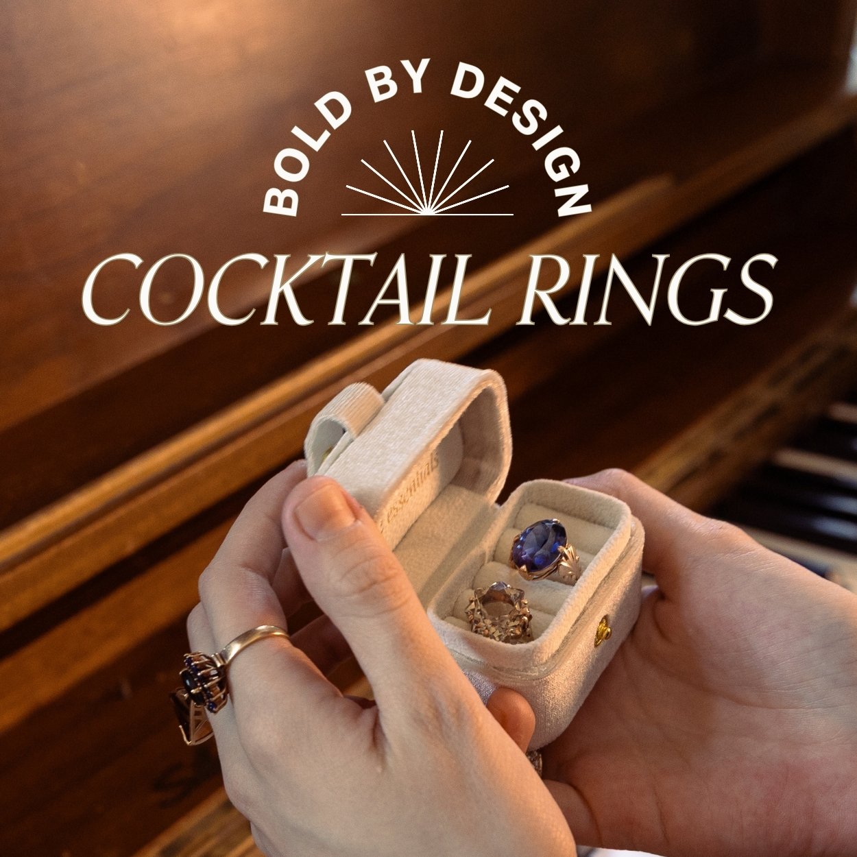 Vintage gemstone cocktail rings in a small box held by hands with a piano in the background. Text overlay reads 'Bold by Design' 'cocktail rings'.