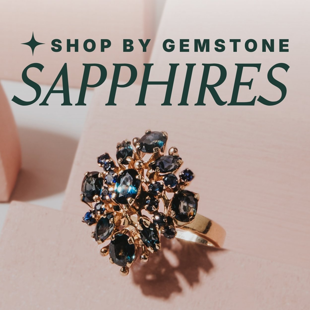 Gold ring with sapphire stones on a pink background, text overlay reads: 'Shop by Gemstone, Sapphires'