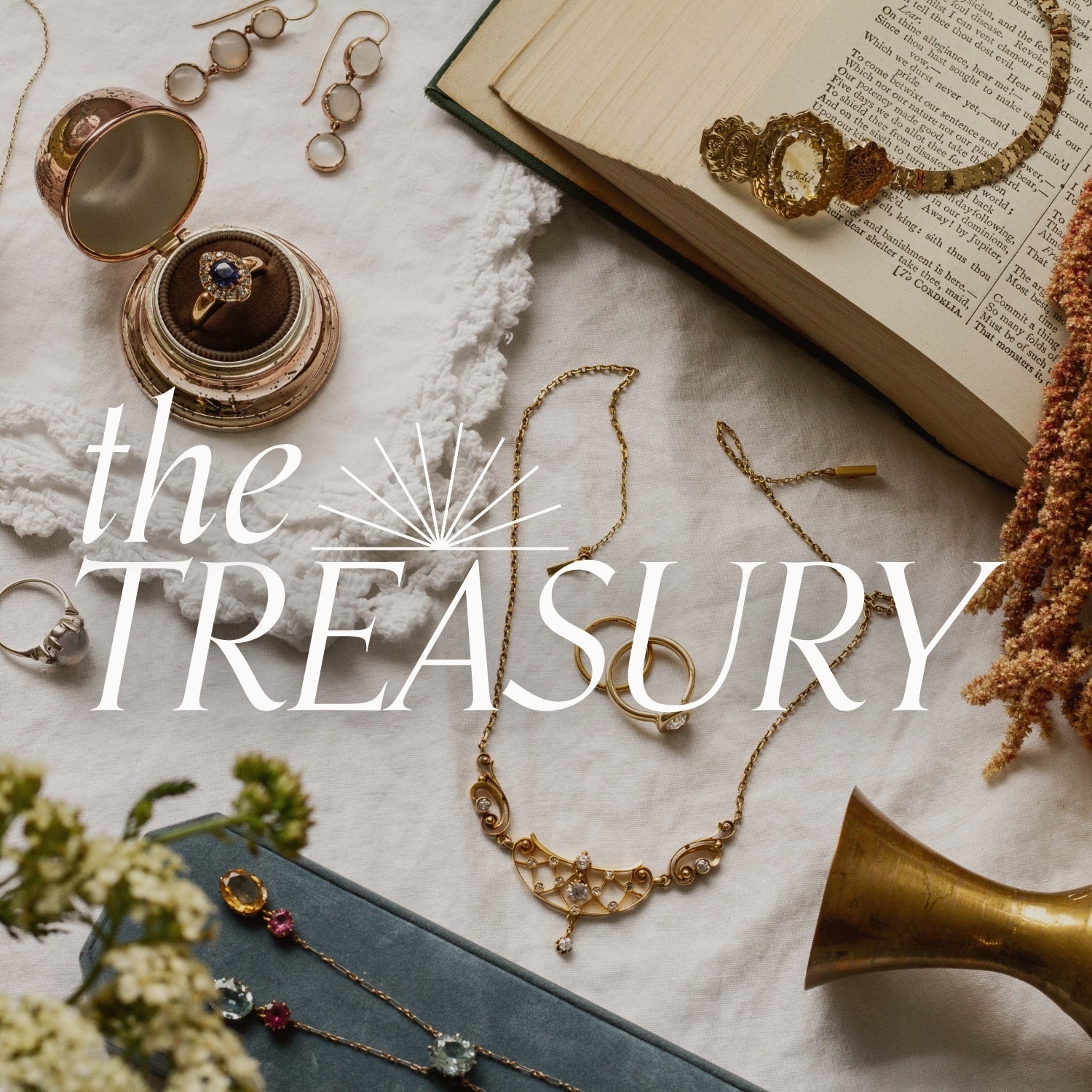 selection of vintage and antique Jewelry including rings and a necklace displayed on a textured fabric surface with vintage styling objects. Text overlay reads: The treasury: curated collection of vintage and antique treasures