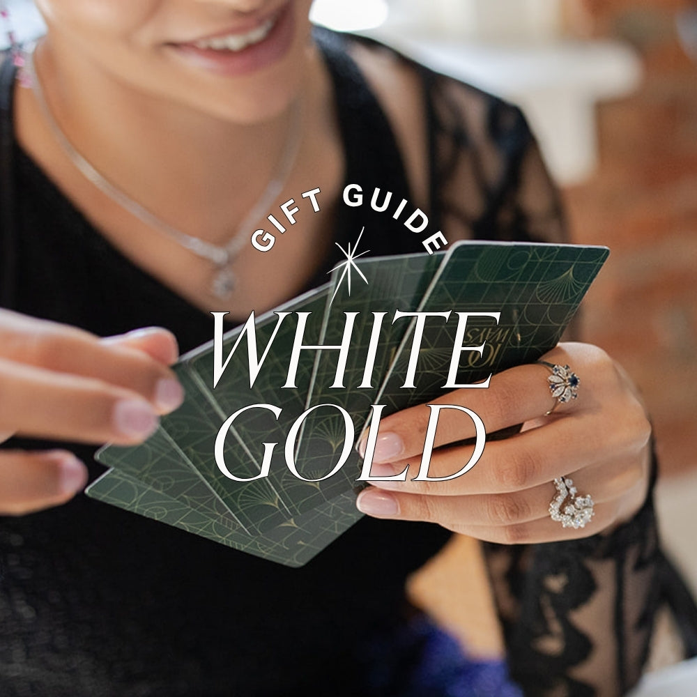 a woman's hands wear white gold and diamond jewellery are seen holding playing cards. text overlay reads gift guide: white gold