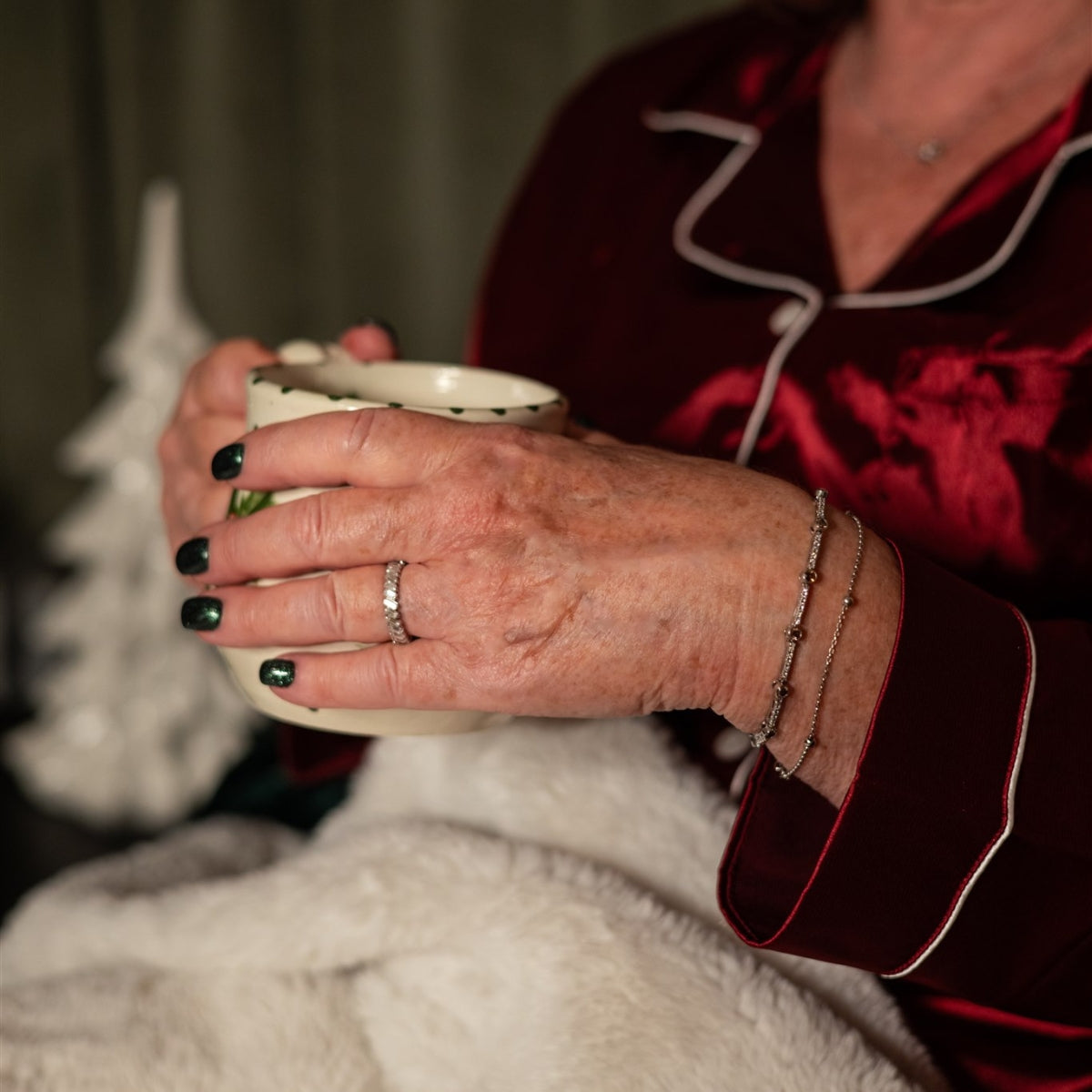 Hand holding holiday mug wearing white gold bracelets and vintage baguette eternity ring