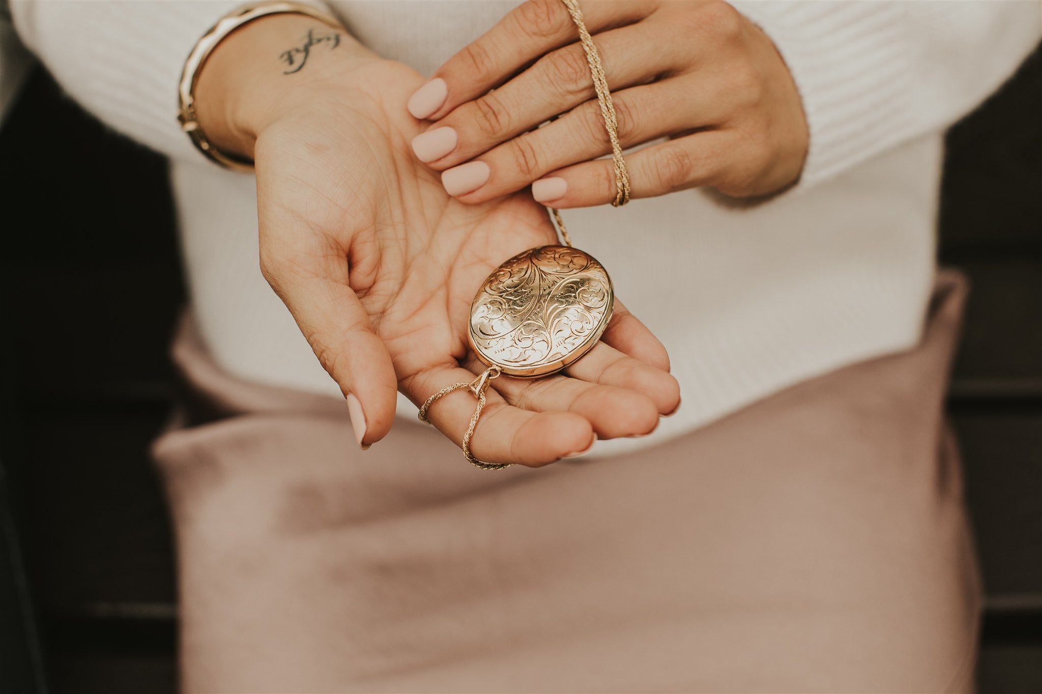 Hand holding a vintage, yellow gold locket with ornate detail design