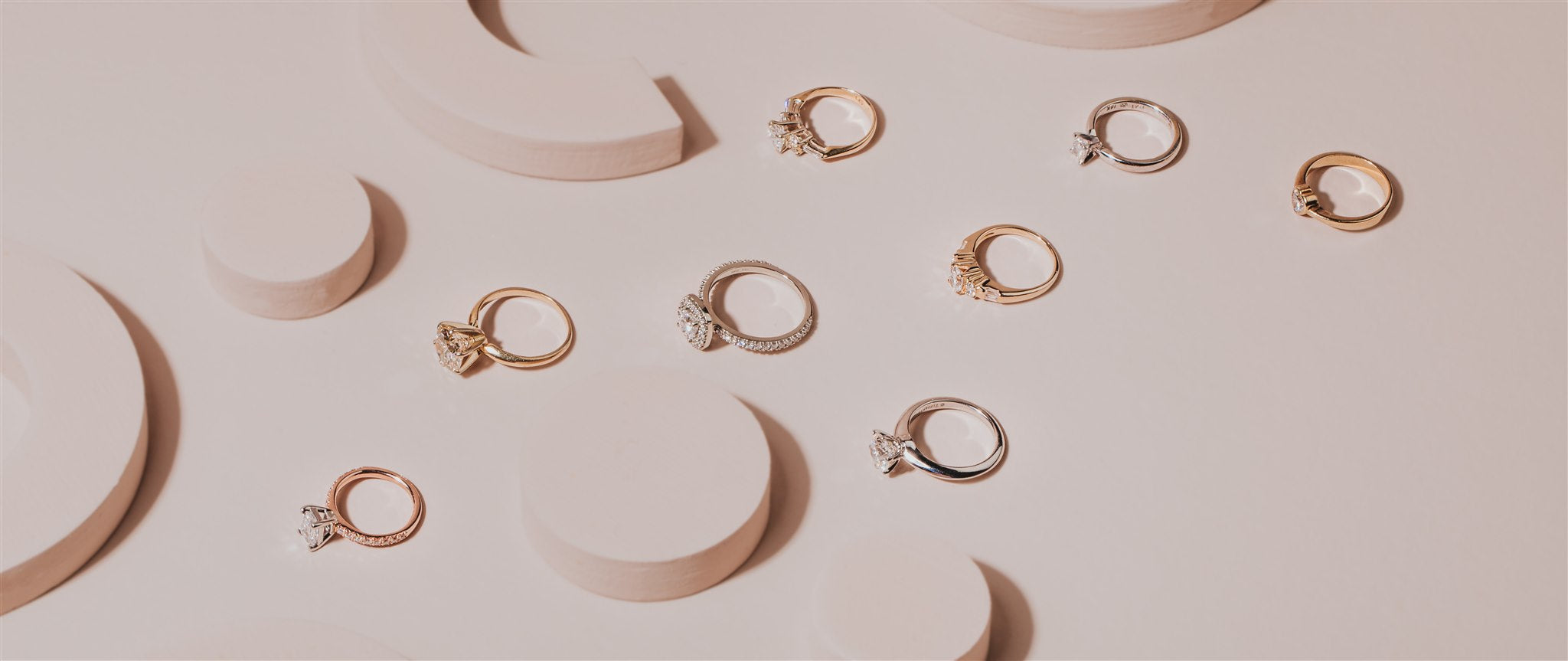 A selection of engagement rings on a light pink background with arch and circle styling props