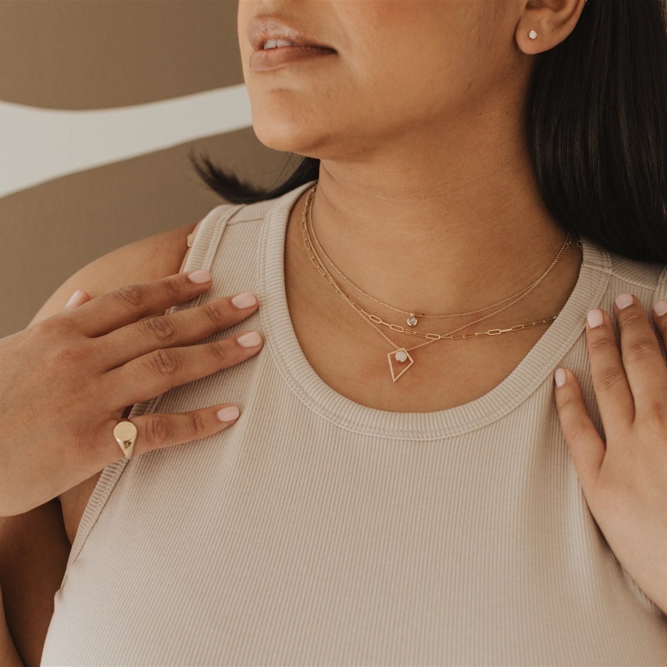 Image up close of woman wearing fine gold jewelry including dainty layered necklaces, diamond stud earrings, and a signet ring