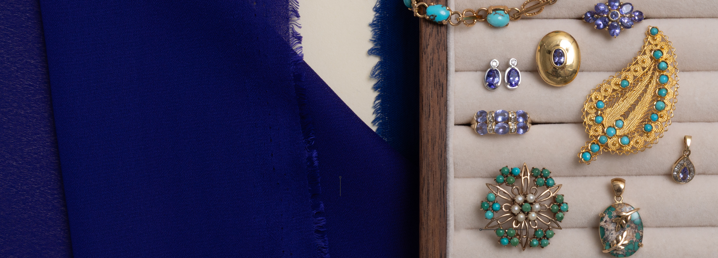 Preloved vintage December birthstone jewellery—tanzanite earrings, turquoise brooches, and blue zircon pendants—displayed on a velvet tray beside rich cobalt fabric.