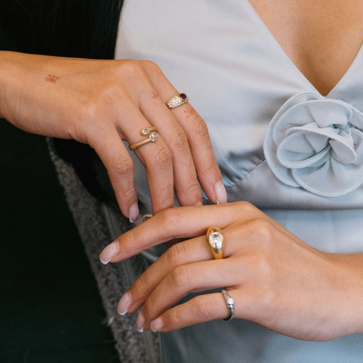 Close-up of a woman's hands wearing multiple yellow gold, vintage rings, including a dome ring with a diamond solitaire, rose cut diamond bypass ring and other diamond ring jewellery.