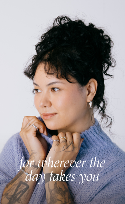 A woman wearing a cozy purple sweater styled with everyday jewellery, including white gold hoop earrings and stacked rings. Text overlay reads: for wherever the day takes you. For everyday, vintage jewellery.