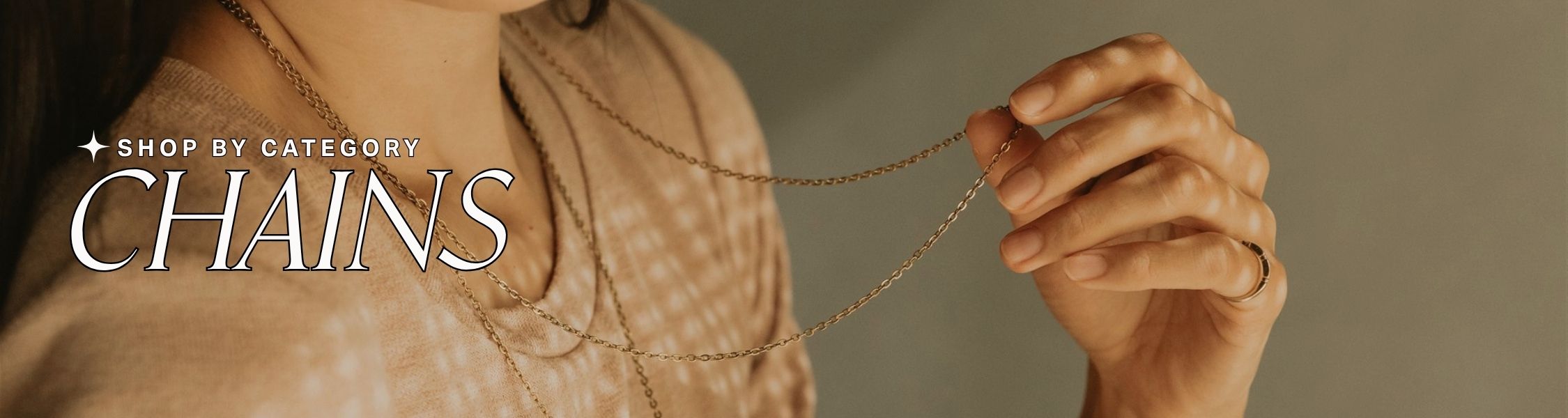 Hand holding a gold chain with 'Shop by Category: Chains' text overlay on a beige background