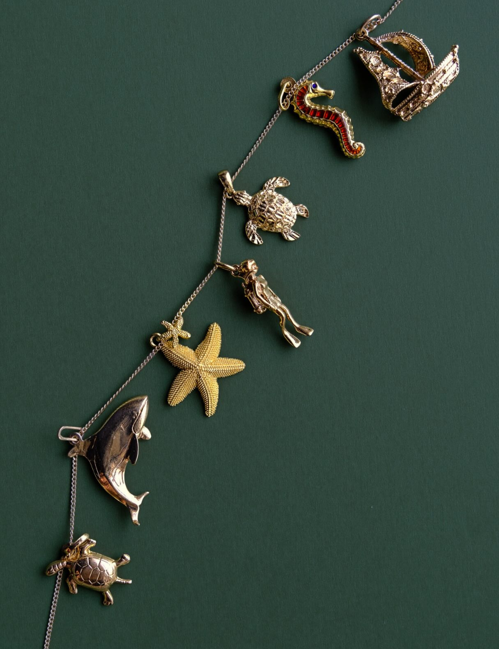 Preloved gold chain necklace featuring nautical sea creature charms including a vintage dolphin, starfish, scuba diver, and sea turtle against a solid green background.