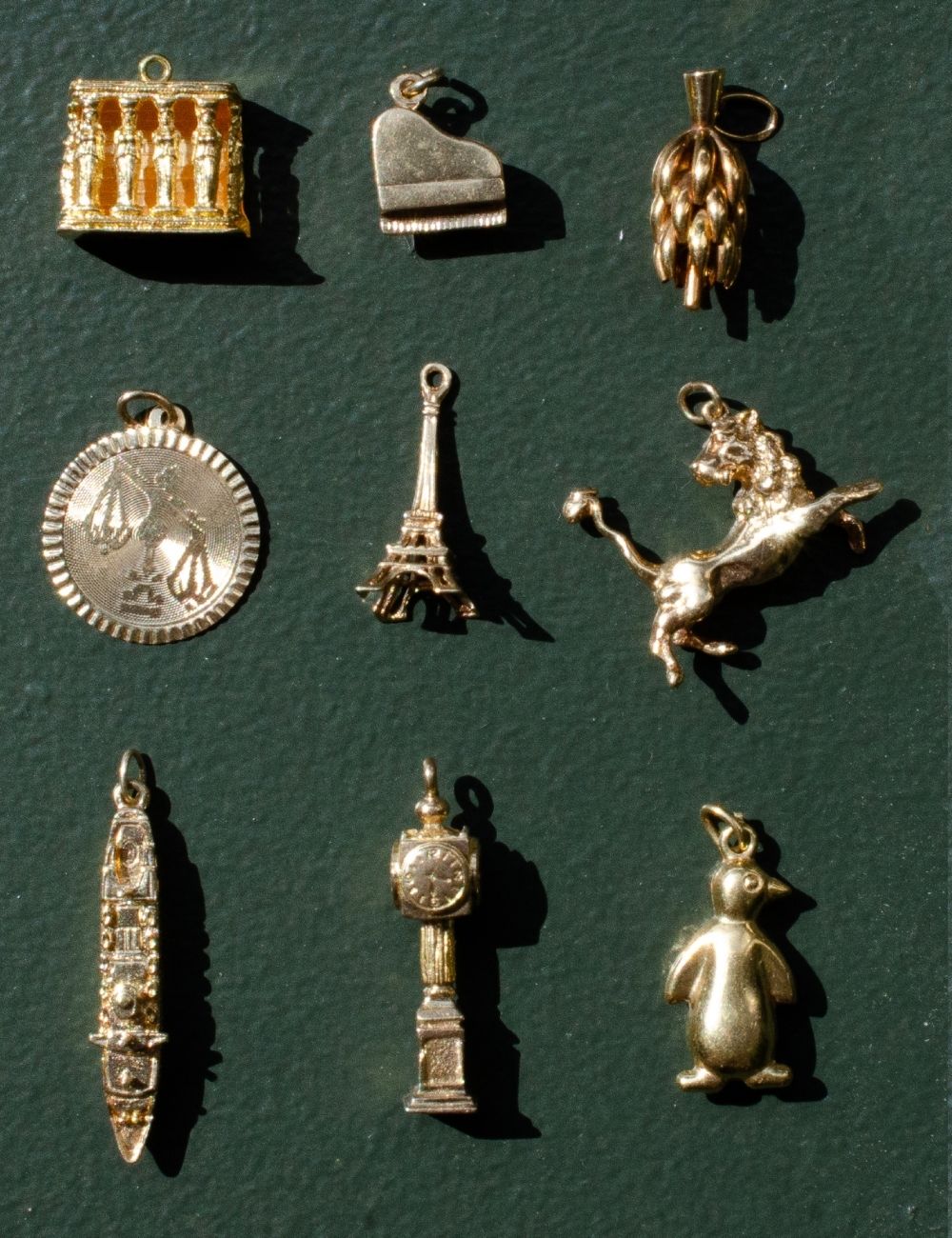 Collection of unique, yellow gold vintage charms on a dark green background