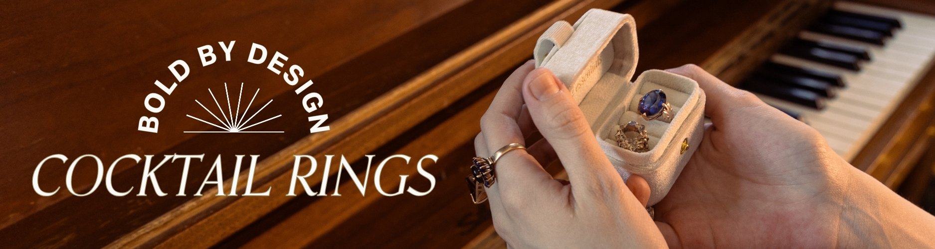 Vintage gemstone cocktail rings in a small box held by hands with a piano in the background. Text overlay reads 'Bold by Design' 'cocktail rings'.