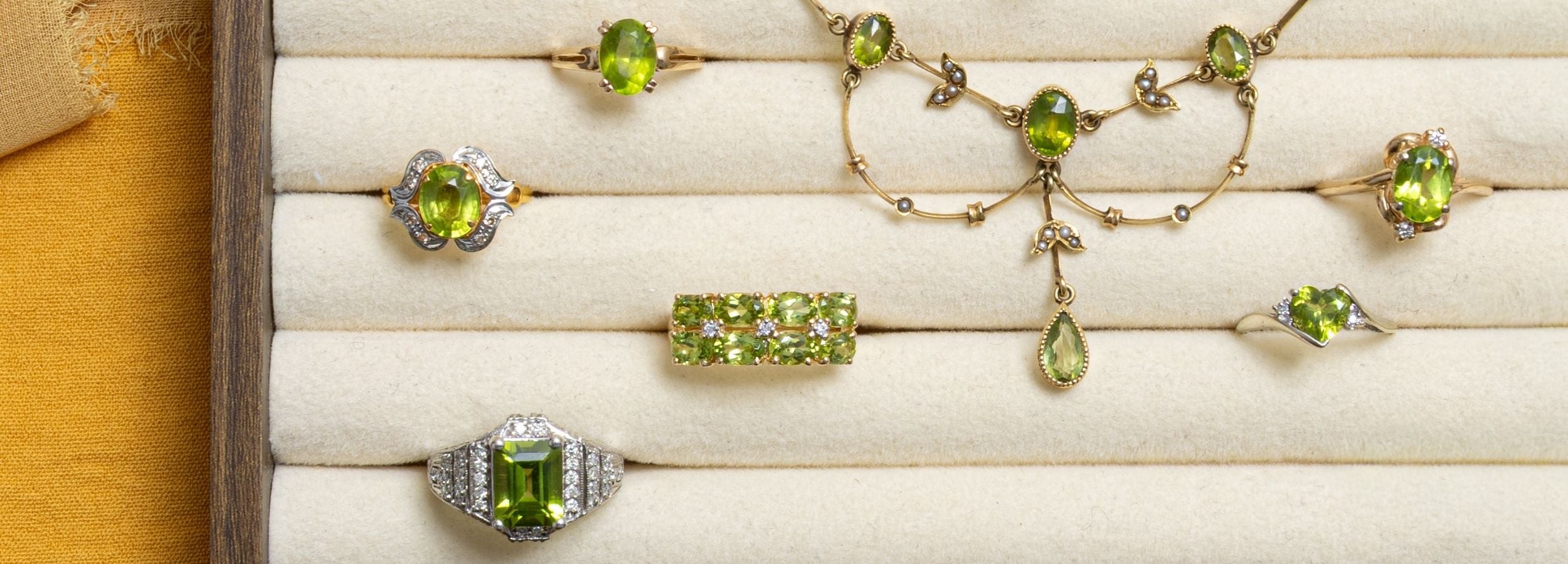 Close up of a jewellery tray featuring an assortment of vintage peridot jewellery, rings and necklace. 